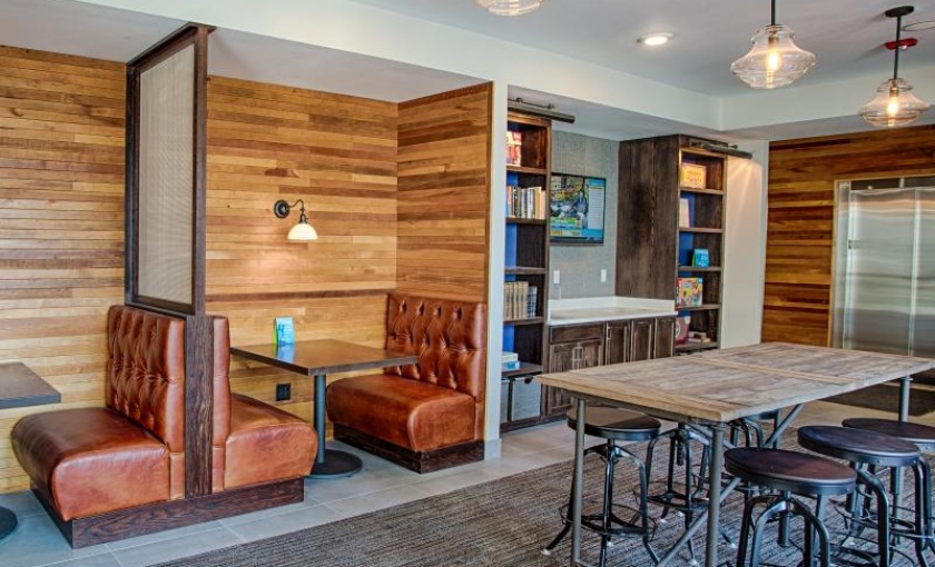 Stylish community space with leather booth seating, a wooden accent wall, and modern lighting at Woodrow Apartments in Fargo, North Dakota.